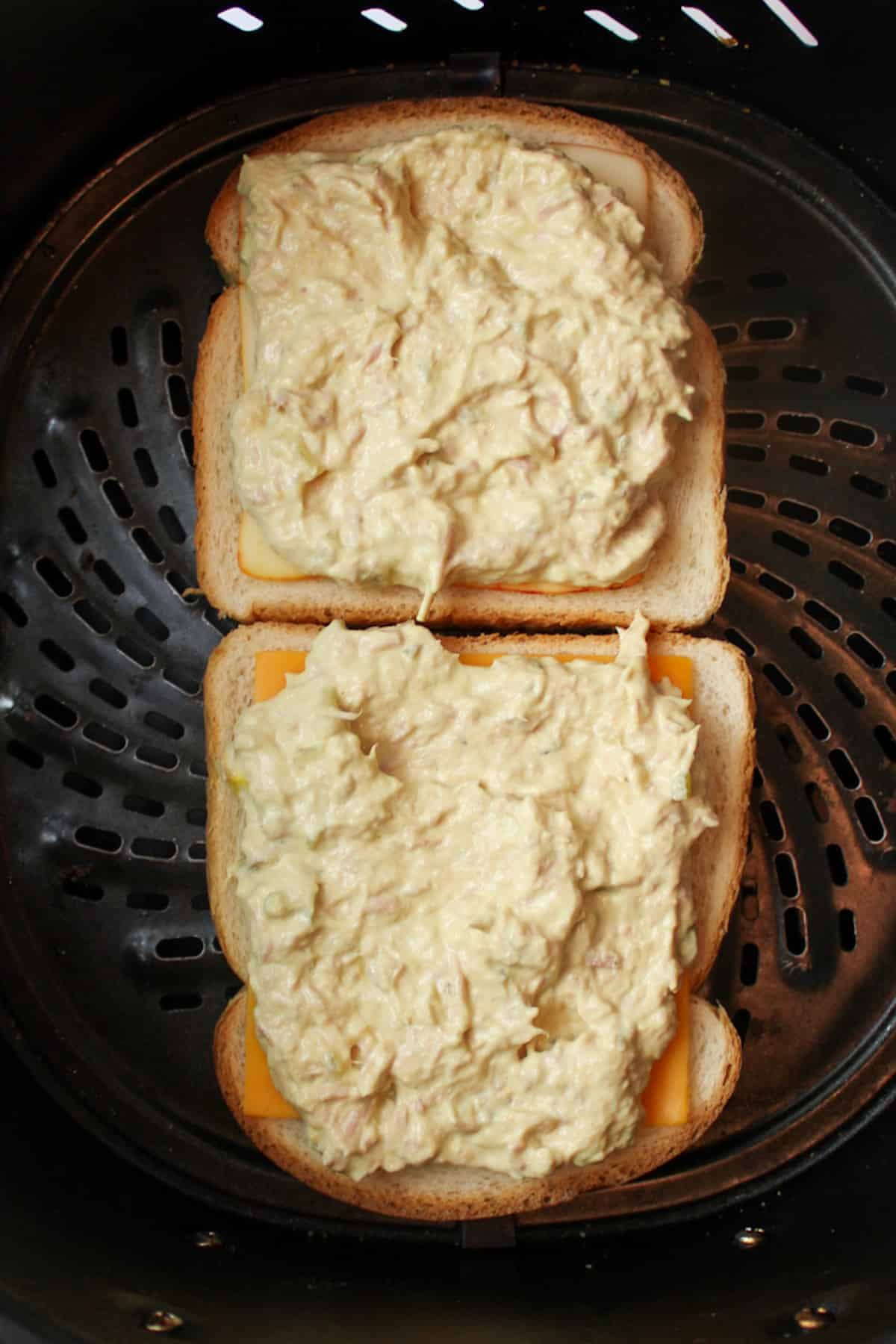 sandwich bread butter side down in an air fryer basket with sliced cheese and tuna filling on top