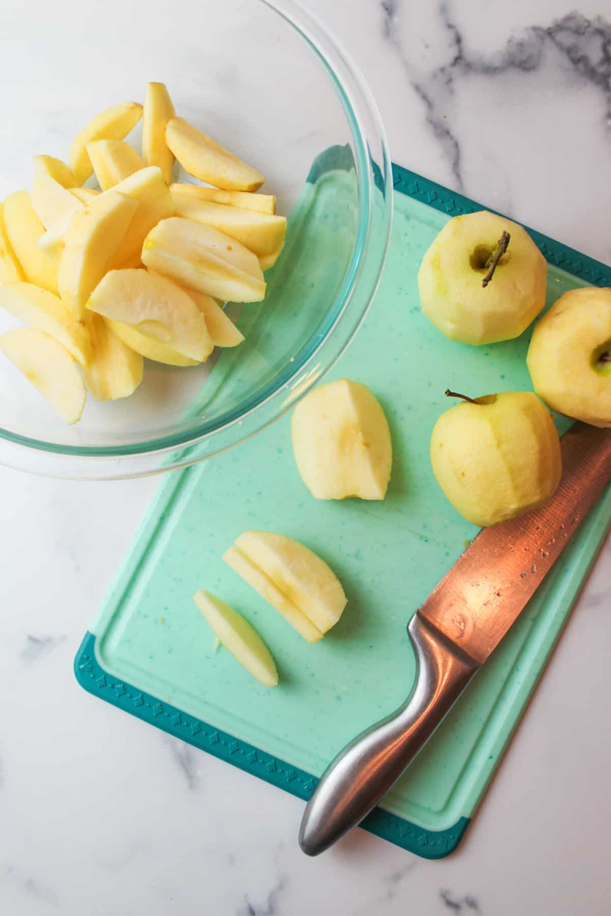sliced apples on a cutting board with a knife and a bowl of apple slices.