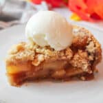 an upclose side view of a slice of apple pie with graham cracker crust and a scoop of vanilla ice cream on top