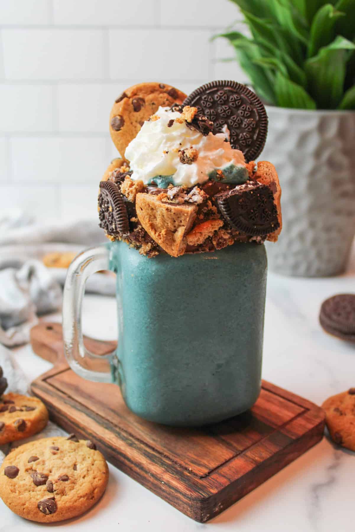 blue monster milkshake topped with whipped cream and cookies with a green leaf plant in the background.