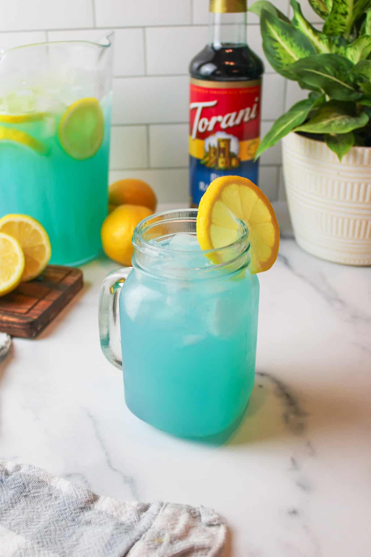 a glass mug full of blue raspberry lemonade and garnished with a slice of lemon