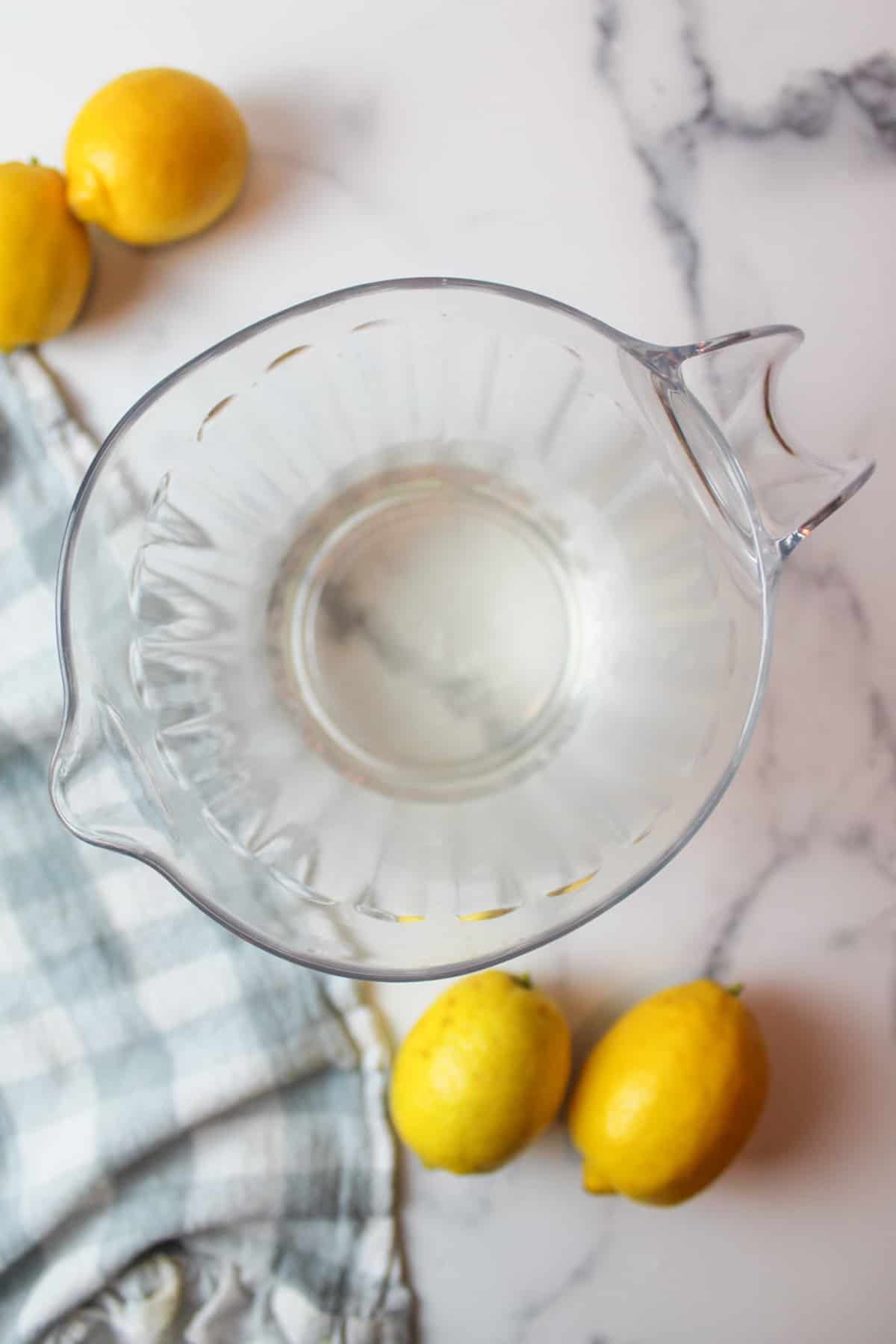 simple syrup at the bottom of a clear pitcher with lemons to the side.