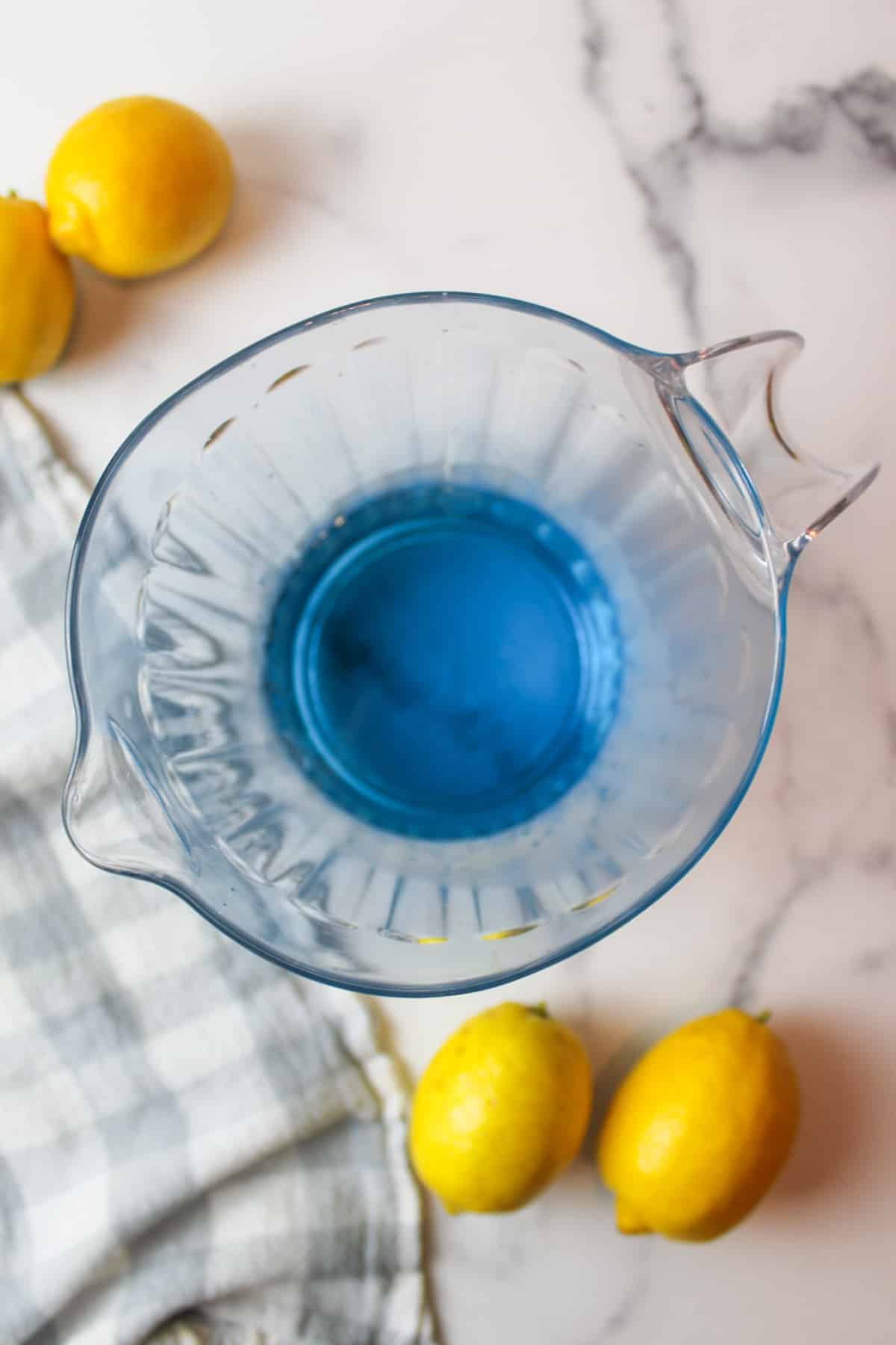 blue syrup added to simple syrup in the bottom of a pitcher with lemons to the sides