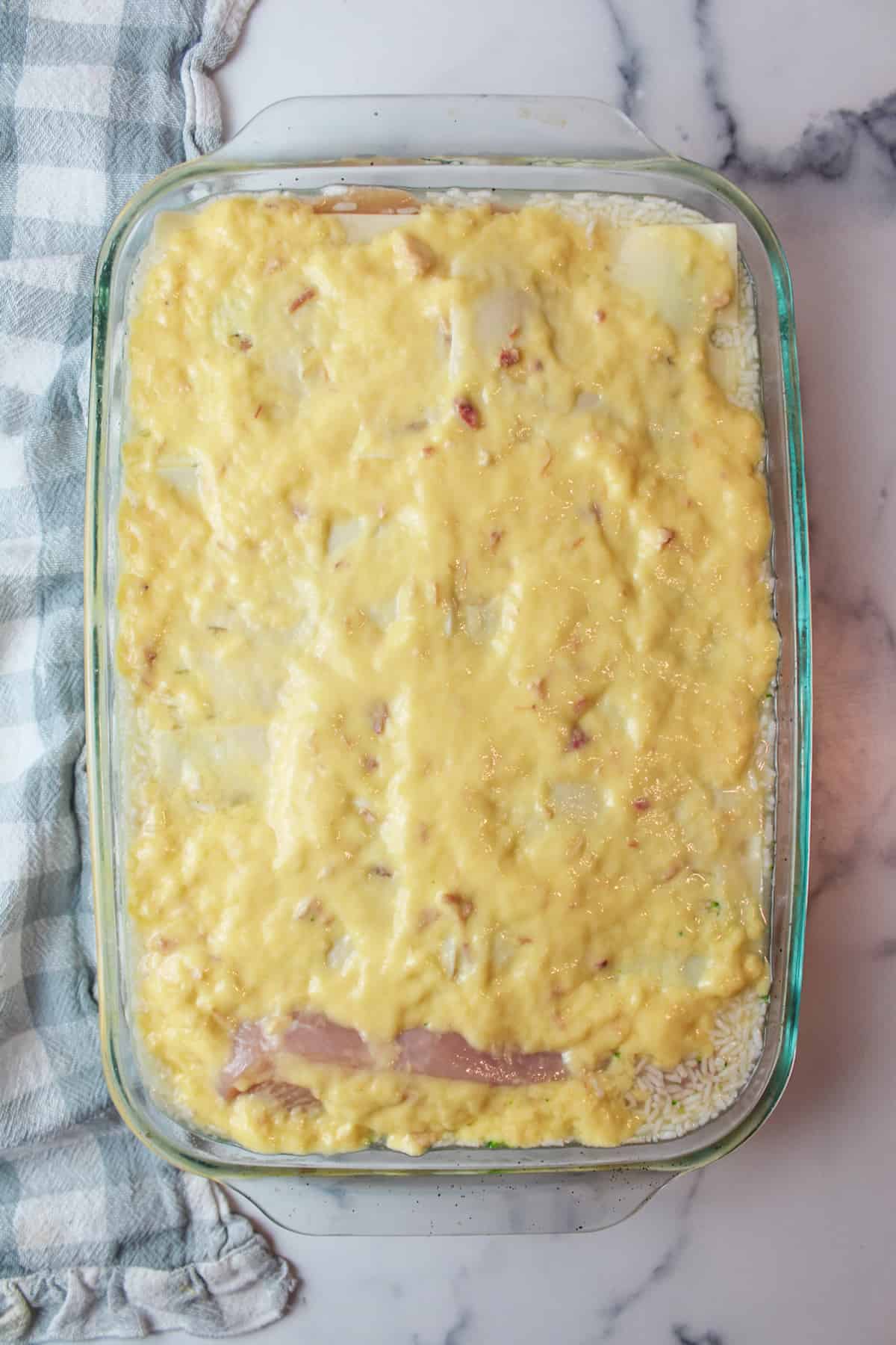 condensed soup spread over swiss cheese slices in baking dish with rice and chicken.