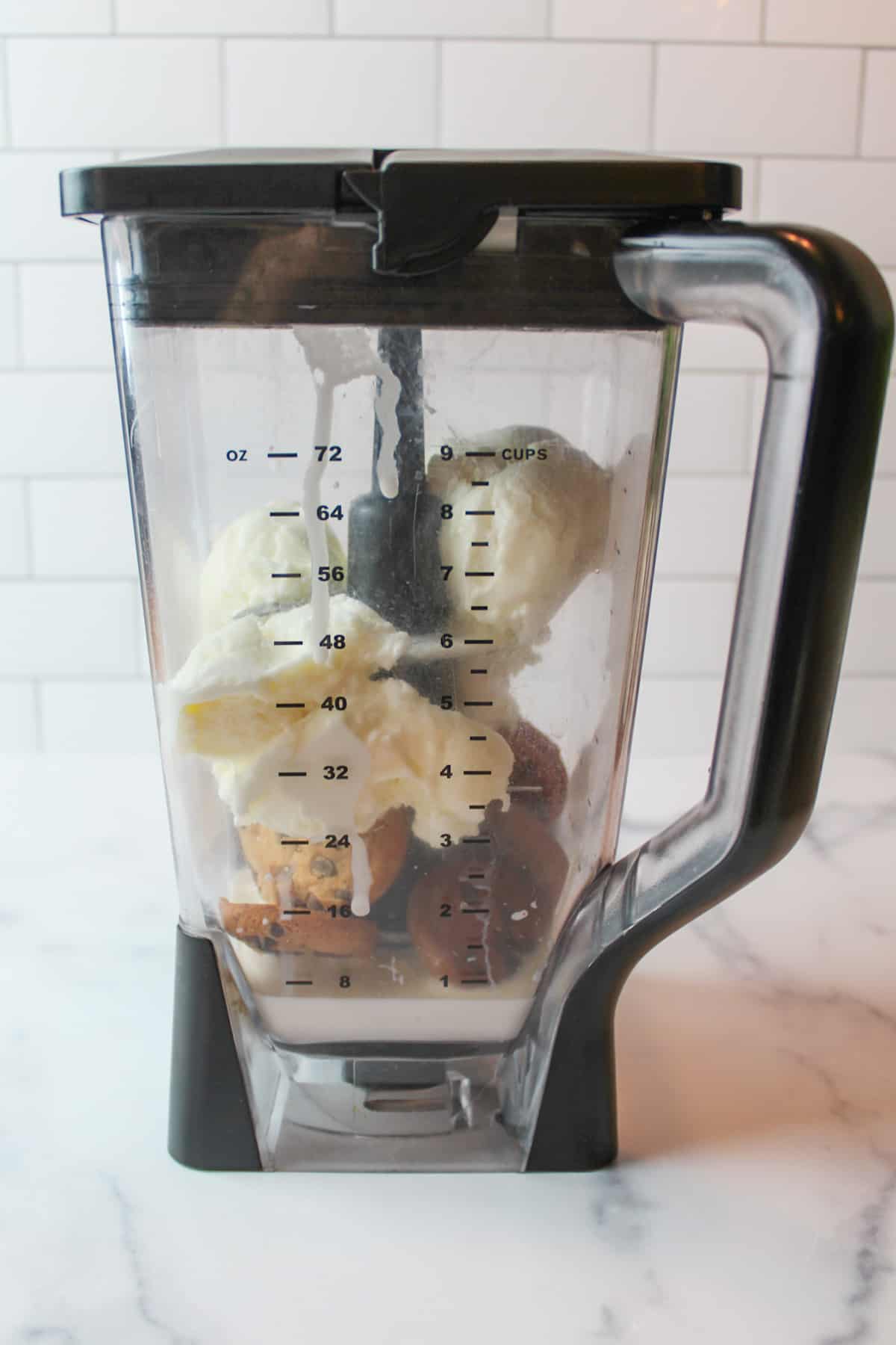 side view of a blender with a lid on holding milk cookies and vanilla ice cream inside