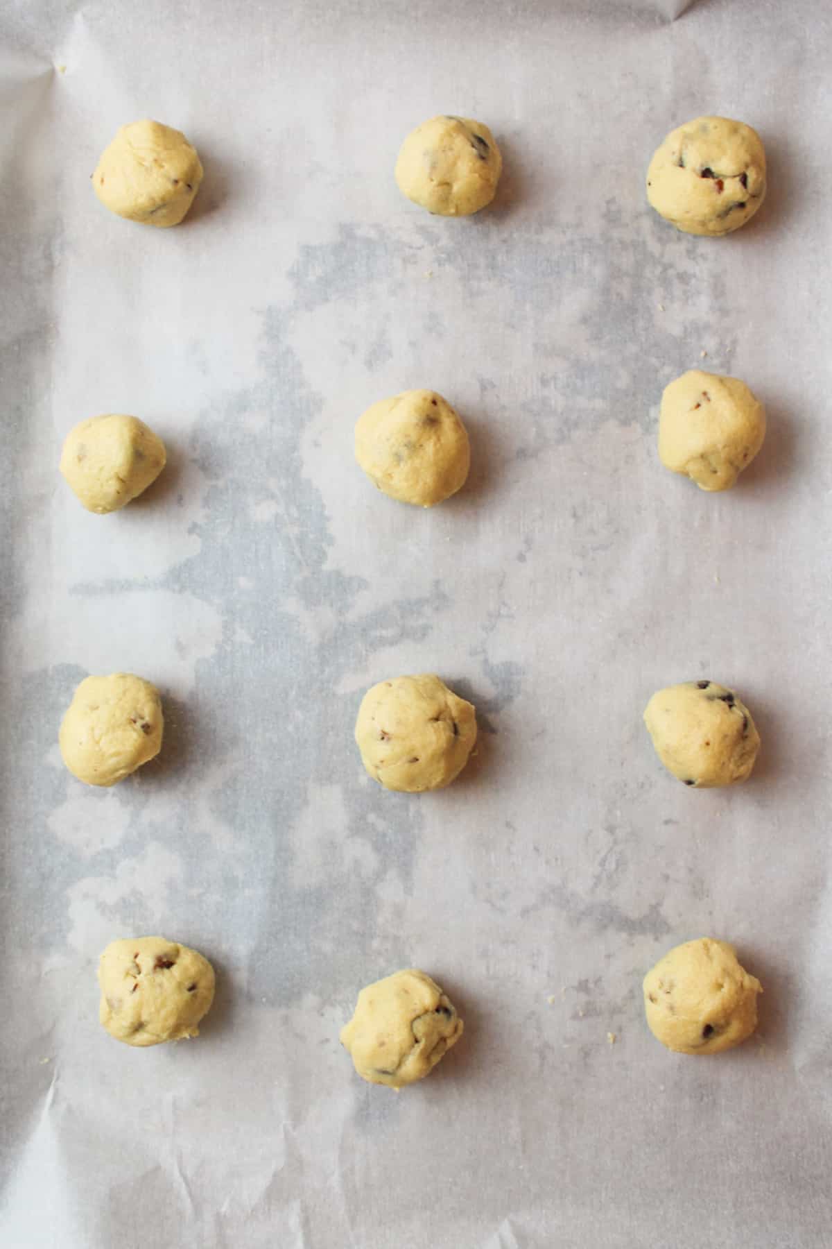 scooped balls of chocolate chip pecan cookie dough on a parchment paper lined baking sheet