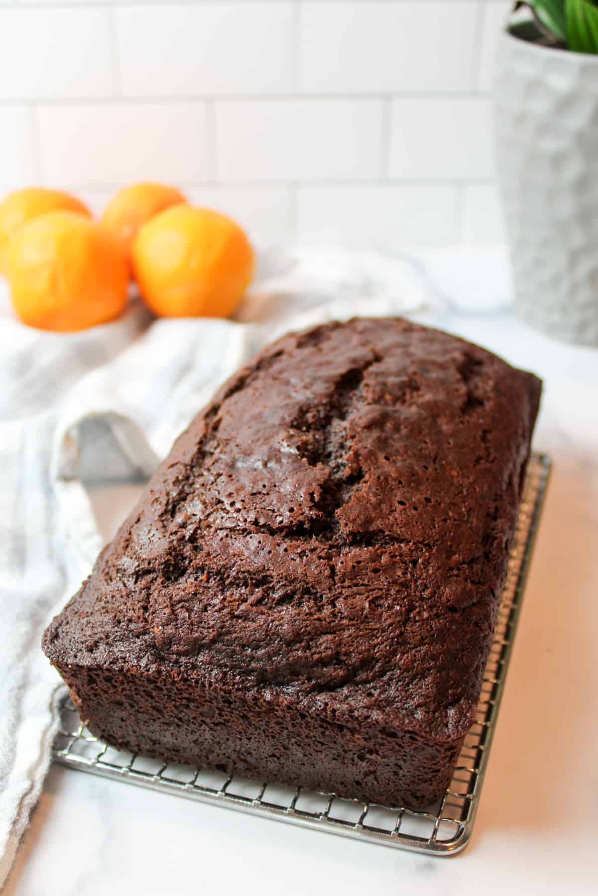 a side view of a loaf of chocoalte orange banana bread on aa iwre rack with fresh oranges in the background