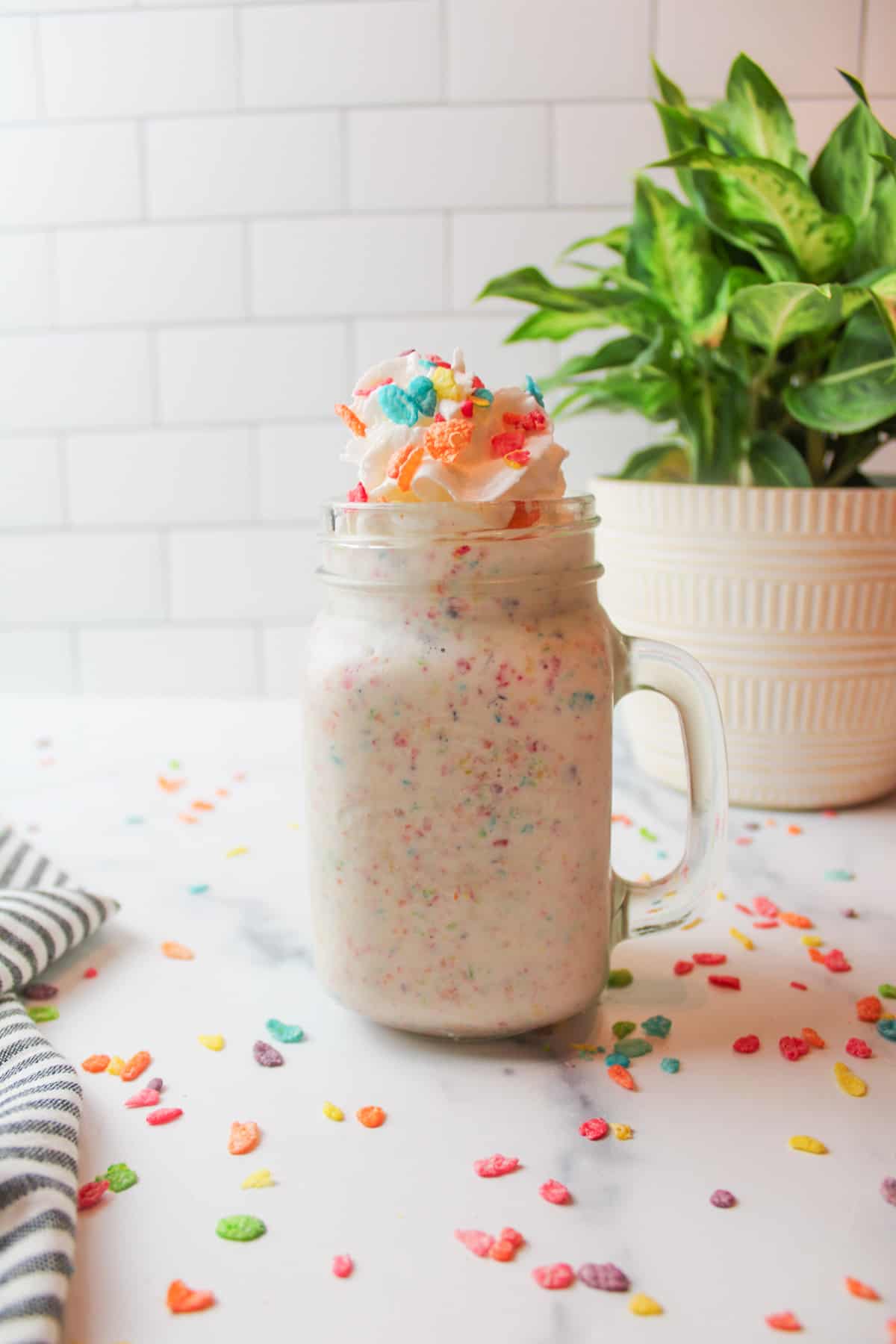 a glass mug full of fruity pebbles milkshake with scattered cereal around it.