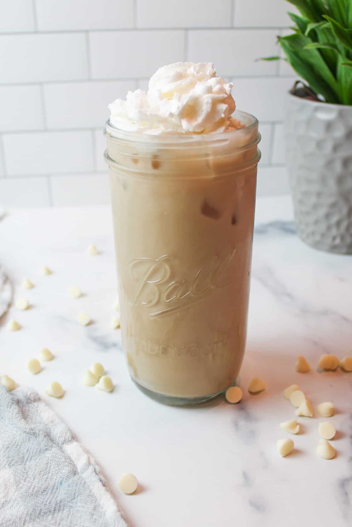 iced white mocha in a tall glass mason jar with whipped cream on top and white chocolate chisp around it