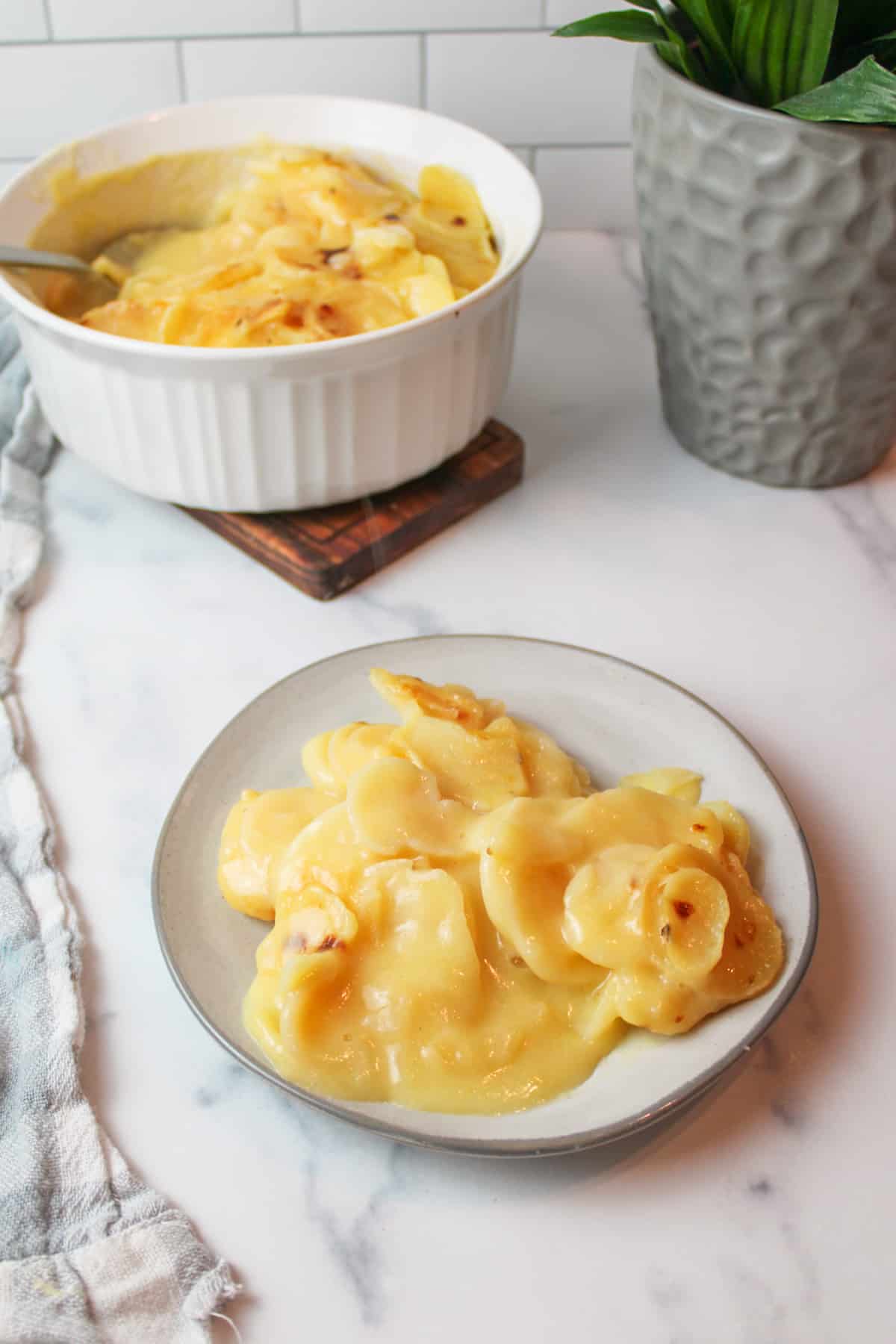 au gratin potatoes on a plate with more in a baking dish in the background.