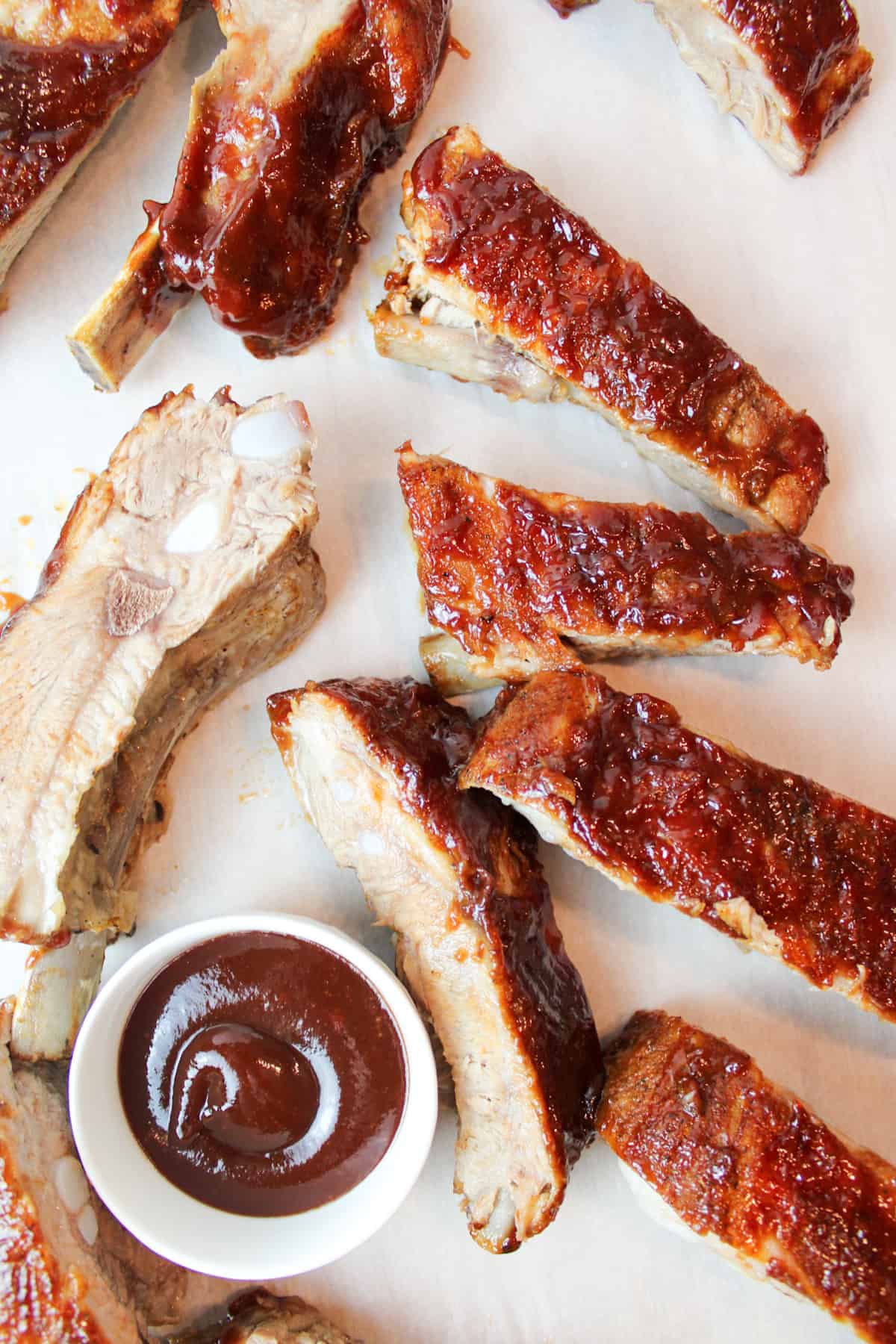 sliced bbq ribs with a small white bowl of bbq sauce.