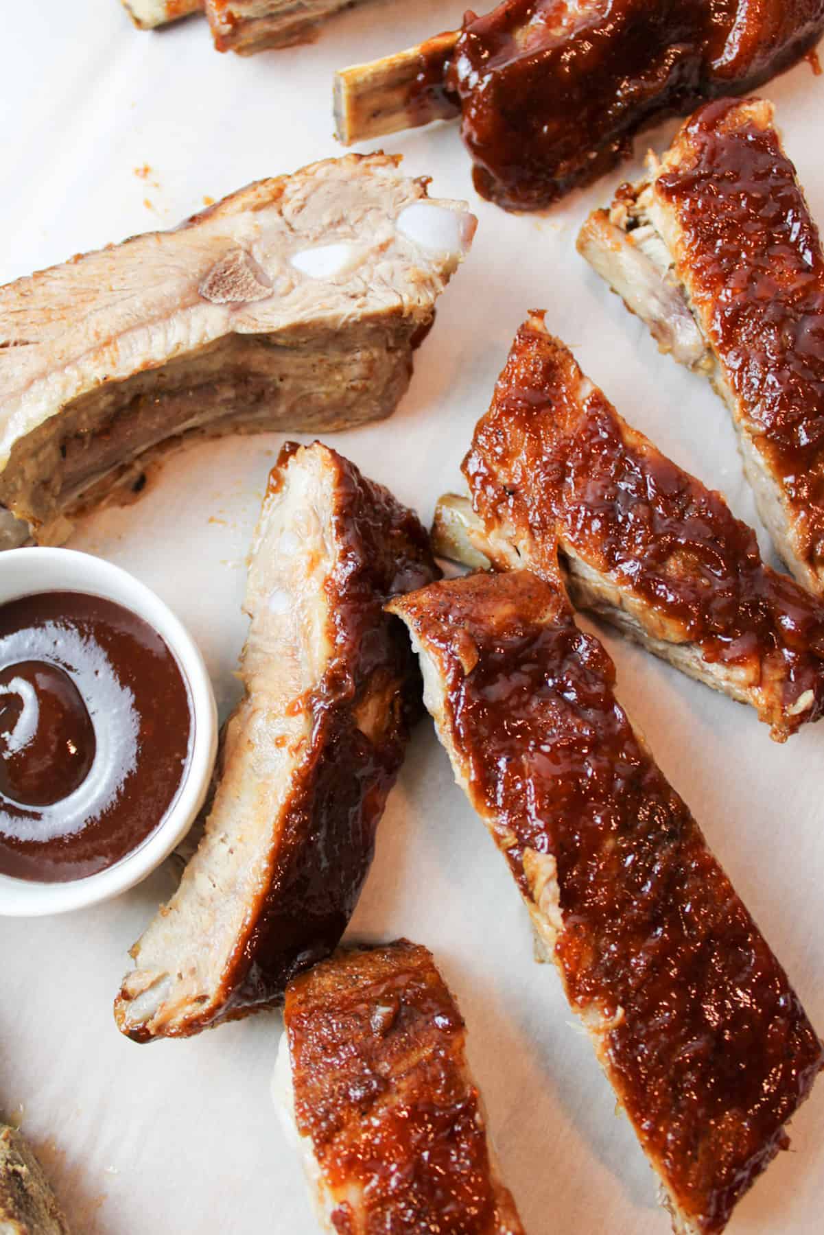 sliced ribs with bbq sauce next to a bowl with more sauce inside