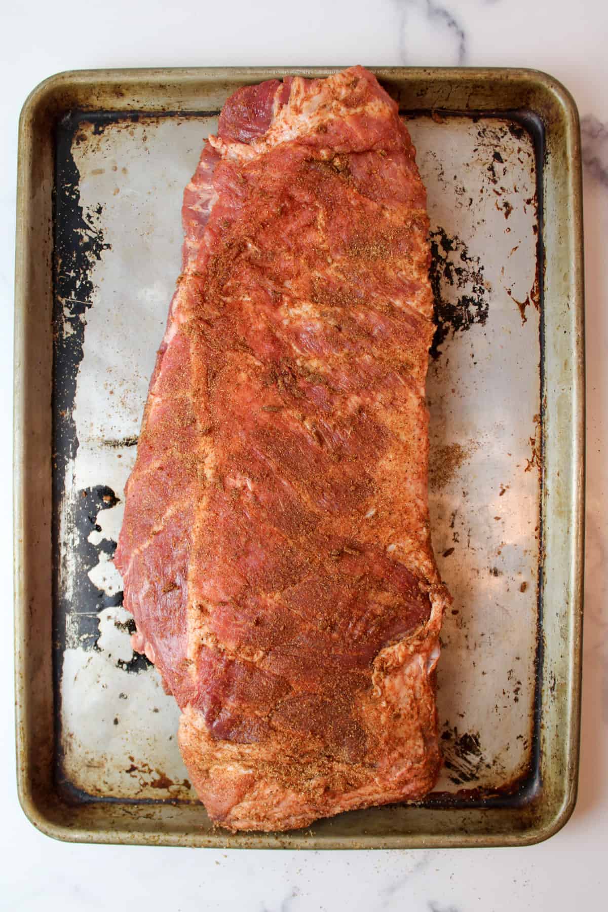 seasonings rubbed over a rack of ribs on a baking sheet.