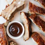 a close up of bbq ribs with a bowl of bbq sauce