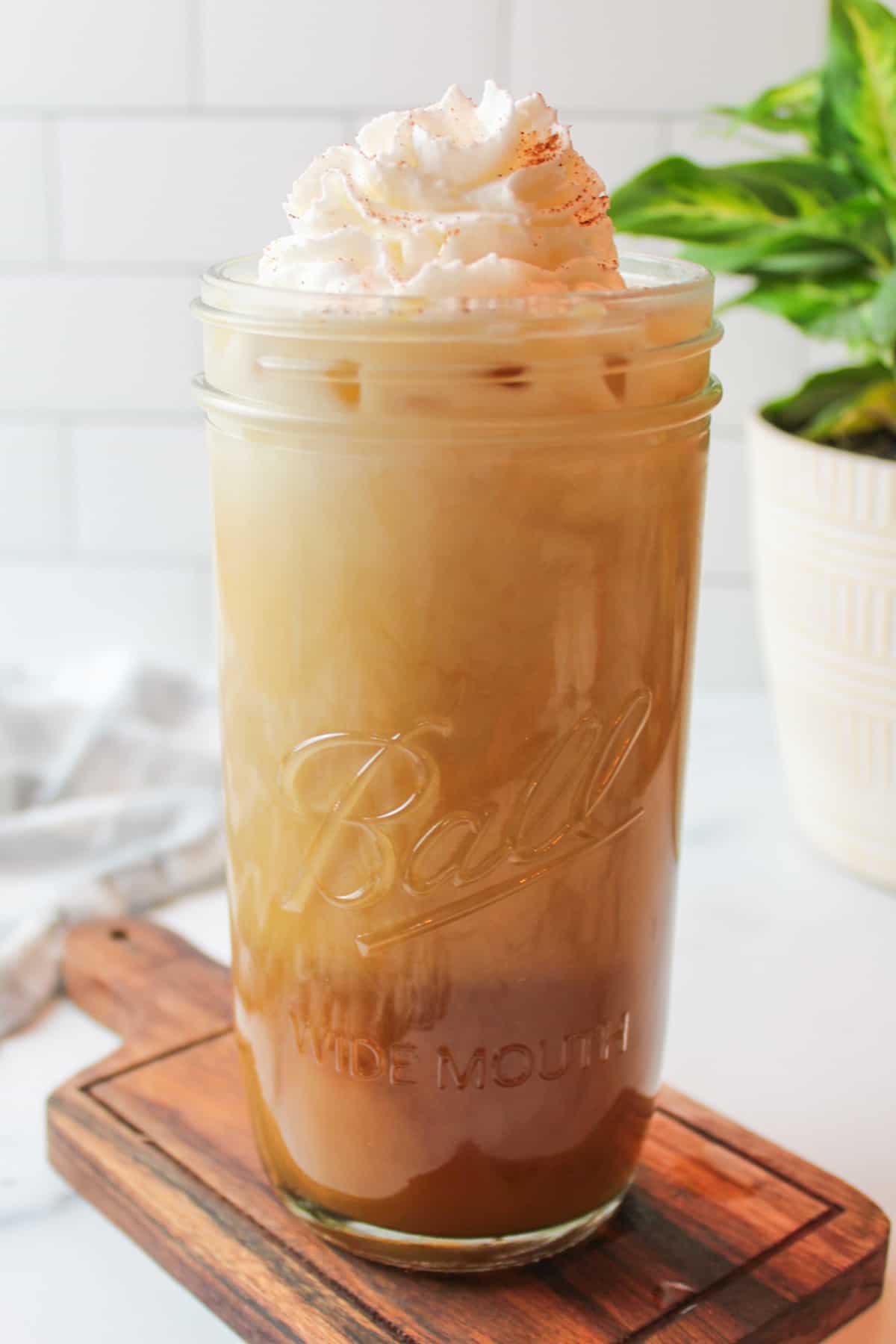 whipped cream topped maple iced coffee in a tall glass cup.