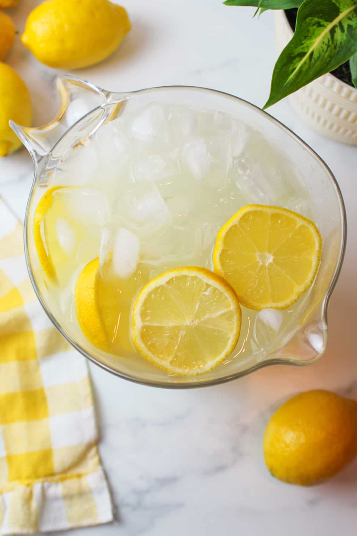 a pitcher full of lemonade and ice with some lemon slices inside.