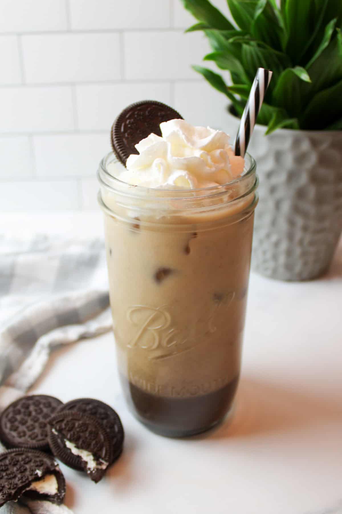 whipped cream and an oreo on a tall glass cup of oreo iced coffee.