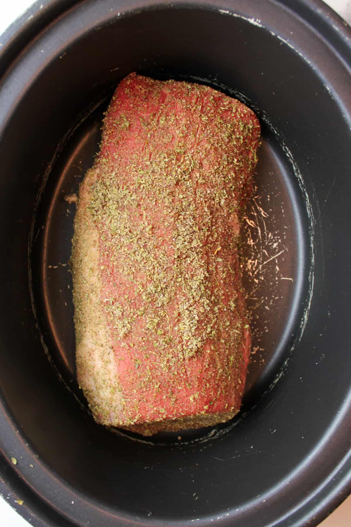 seasoning coated raw beef roast in crock pot