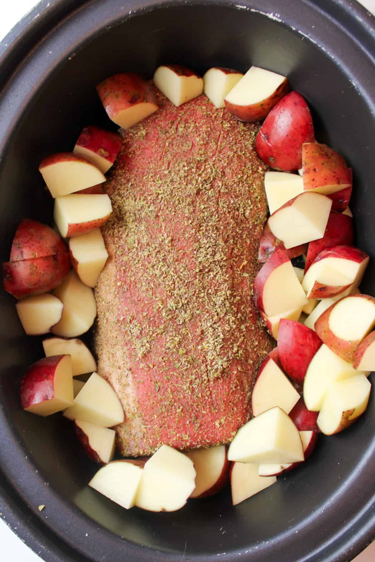 chopped red potatoes and seasoned beef roast in crock pot