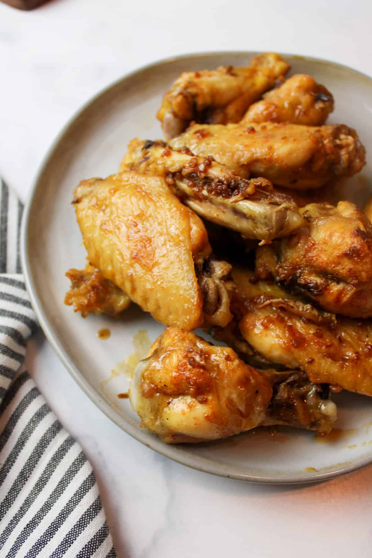 a close up of a plate filled with soy garlic chicken wings next to a striped towel