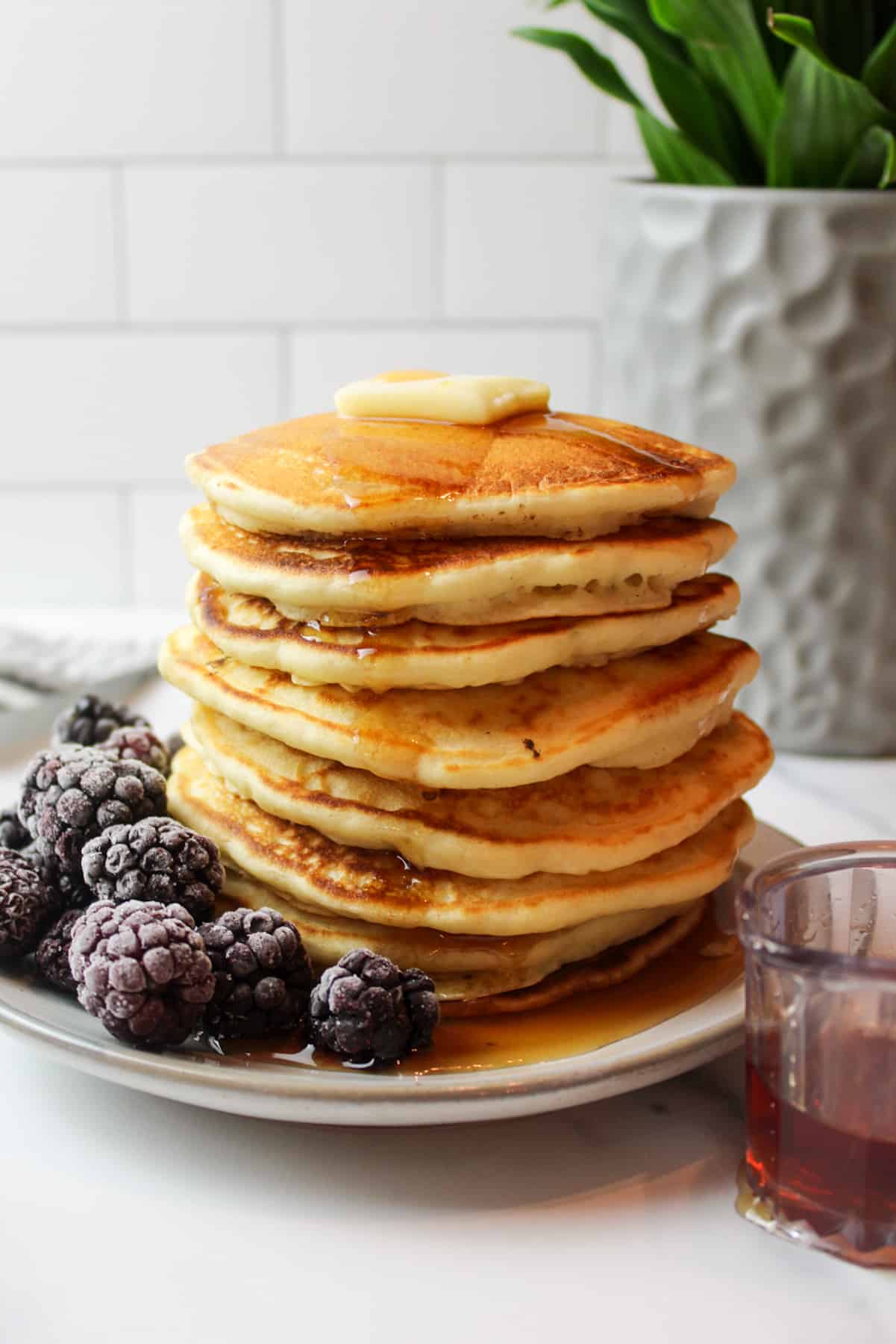 a tall stack of pancakes topped with butter and syrup and with frozen blackberries to the side