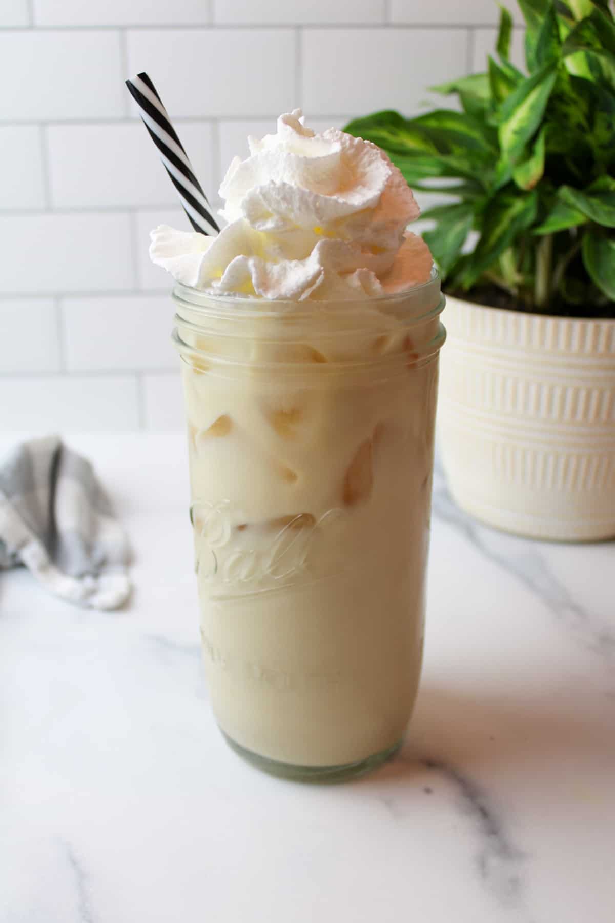 a tall cup full of vanilla iced latte topped with whipped cream.