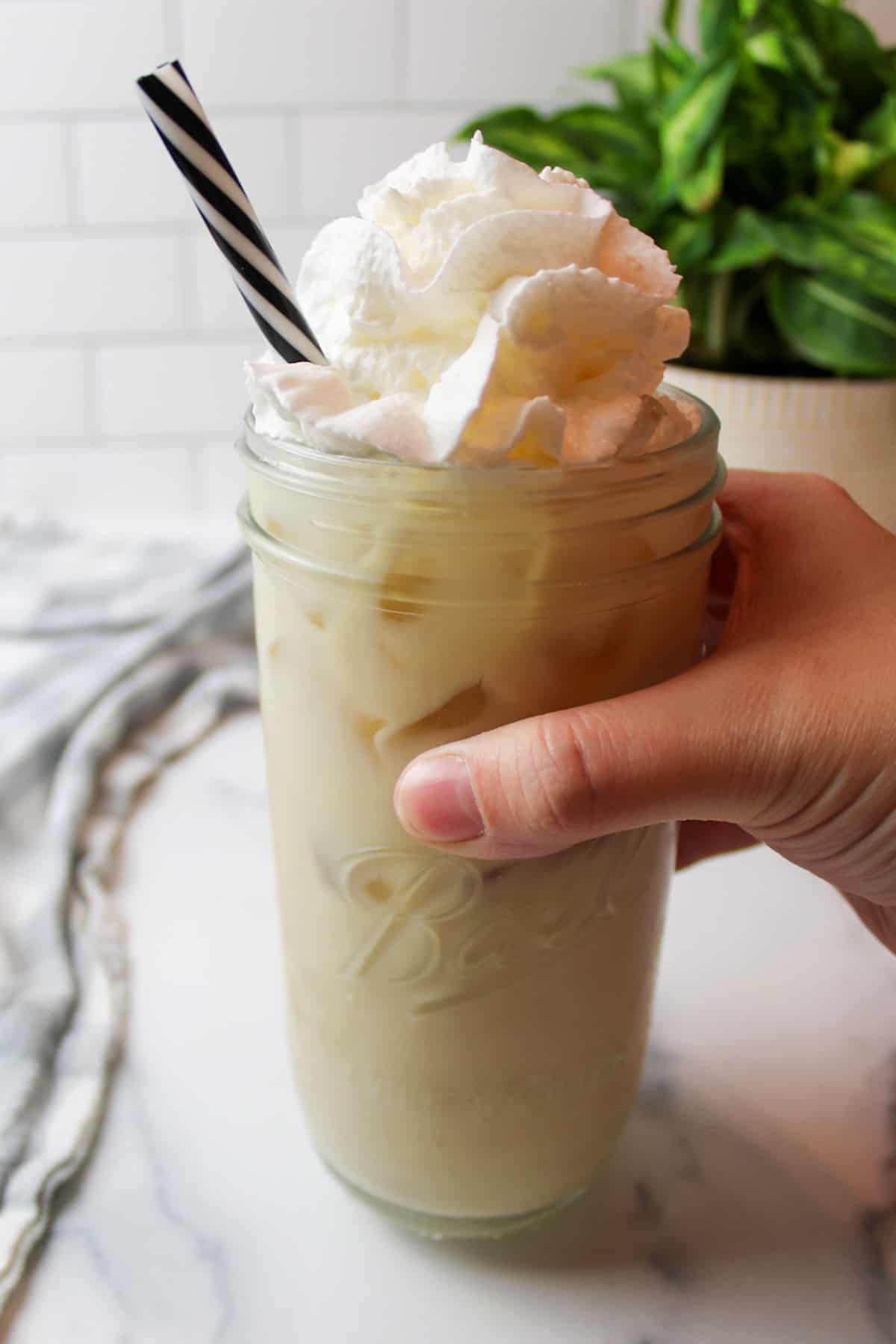 a hand holding a tall glass cup filled with vanilla iced latte.