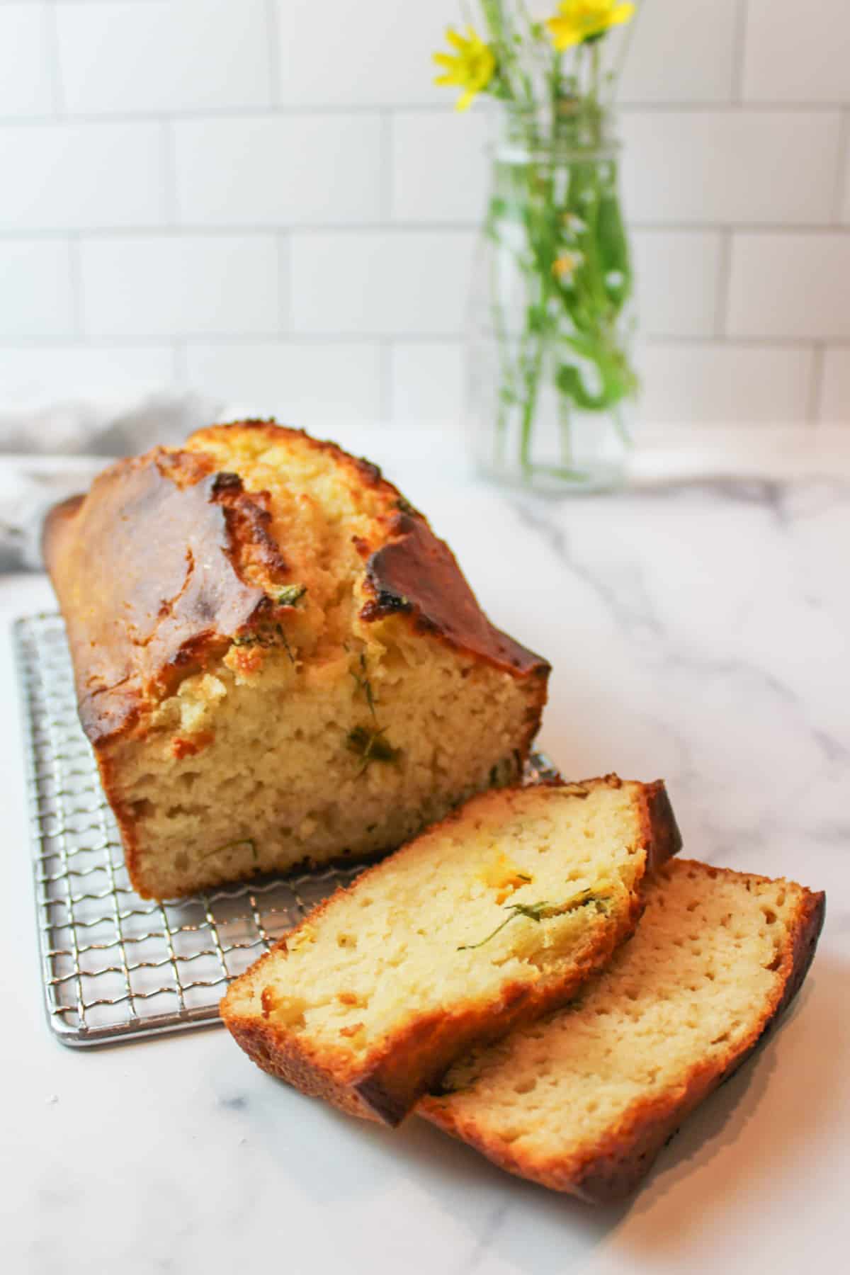 a sliced loaf of dandelion bread on a wire rack.