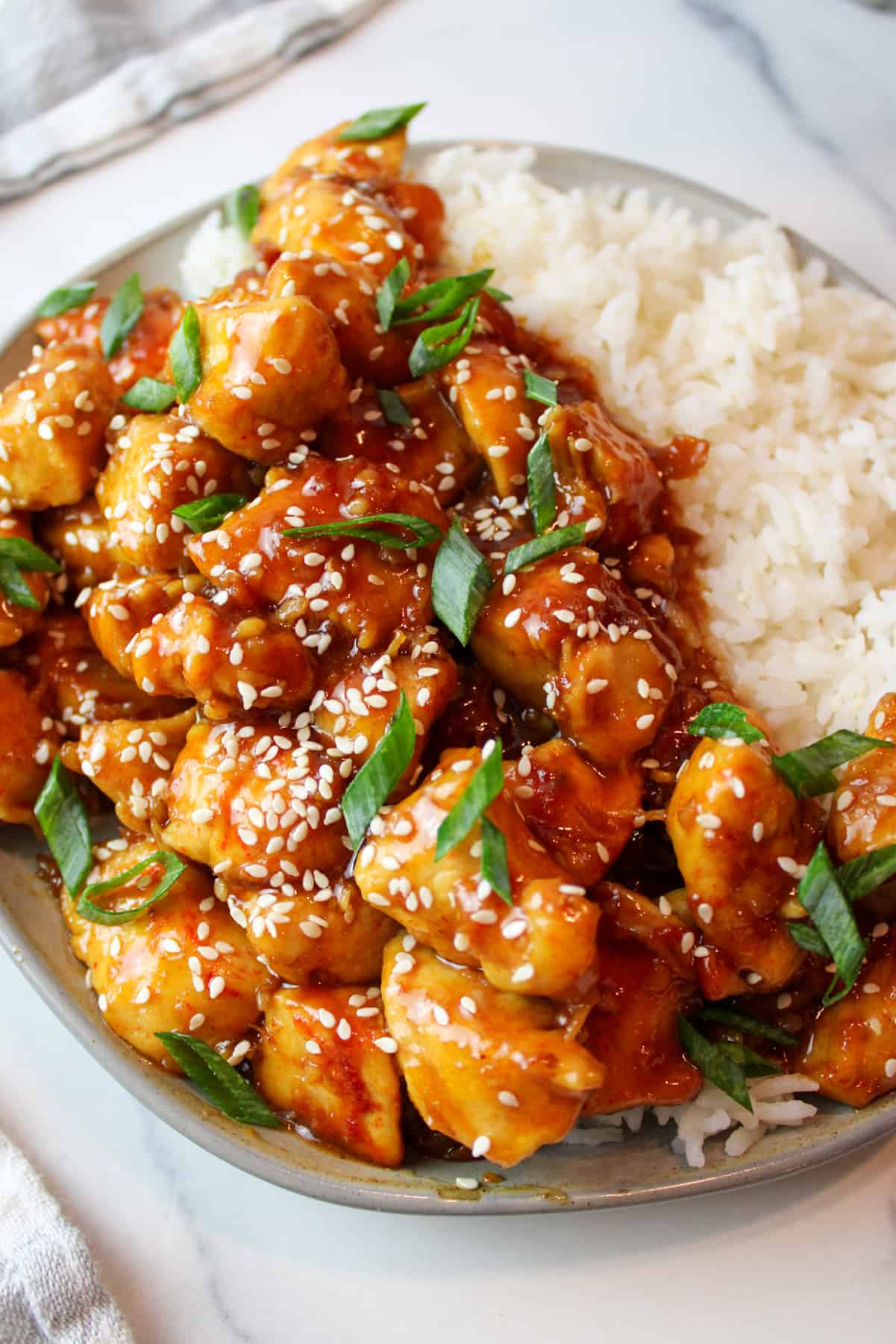 Plate of honey soy chicken bites with sesame seeds and green onions, served with white rice.