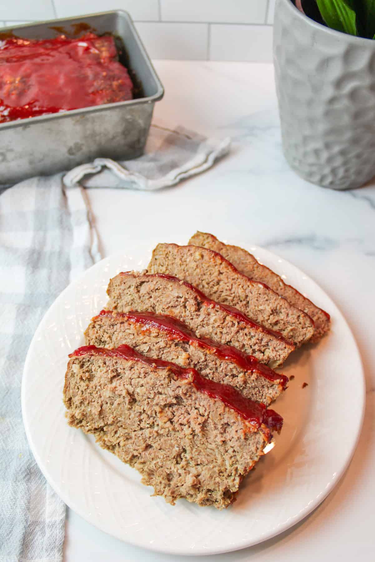 A plate of meatloaf with more in a loaf pan in background.