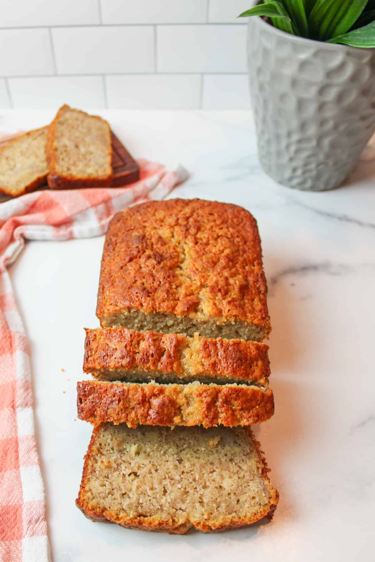 sliced banana bread with slices in the background a pink towel to the side and a plant in the background