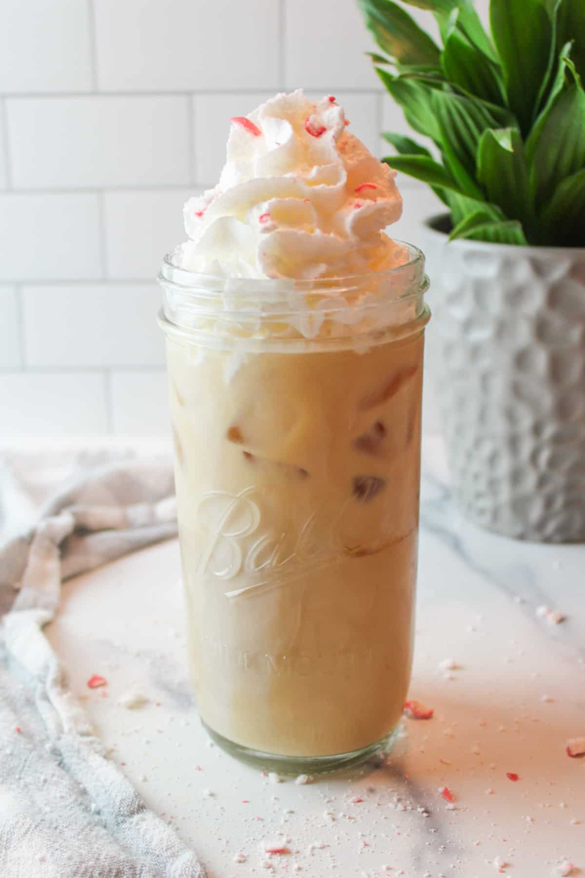 a tall glass cup full of peppermint iced coffee topped with whipped cream and peppermint pieces.