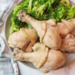 a pile of chicken legs on a plate with steamed broccoli.