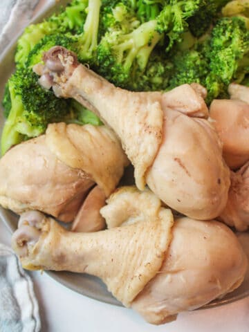 an upclose view of a pile of chicken legs on a plate with steamed broccoli