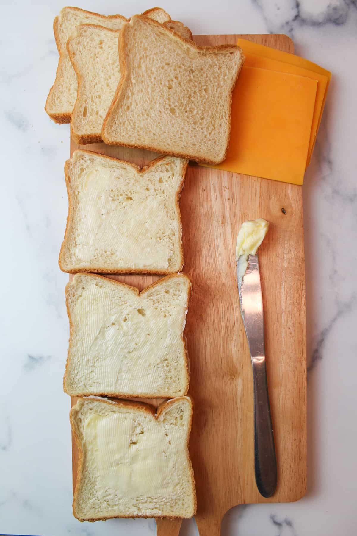 three slices of buttered bread, sandwich bread cheese and a butter covered butterknife.