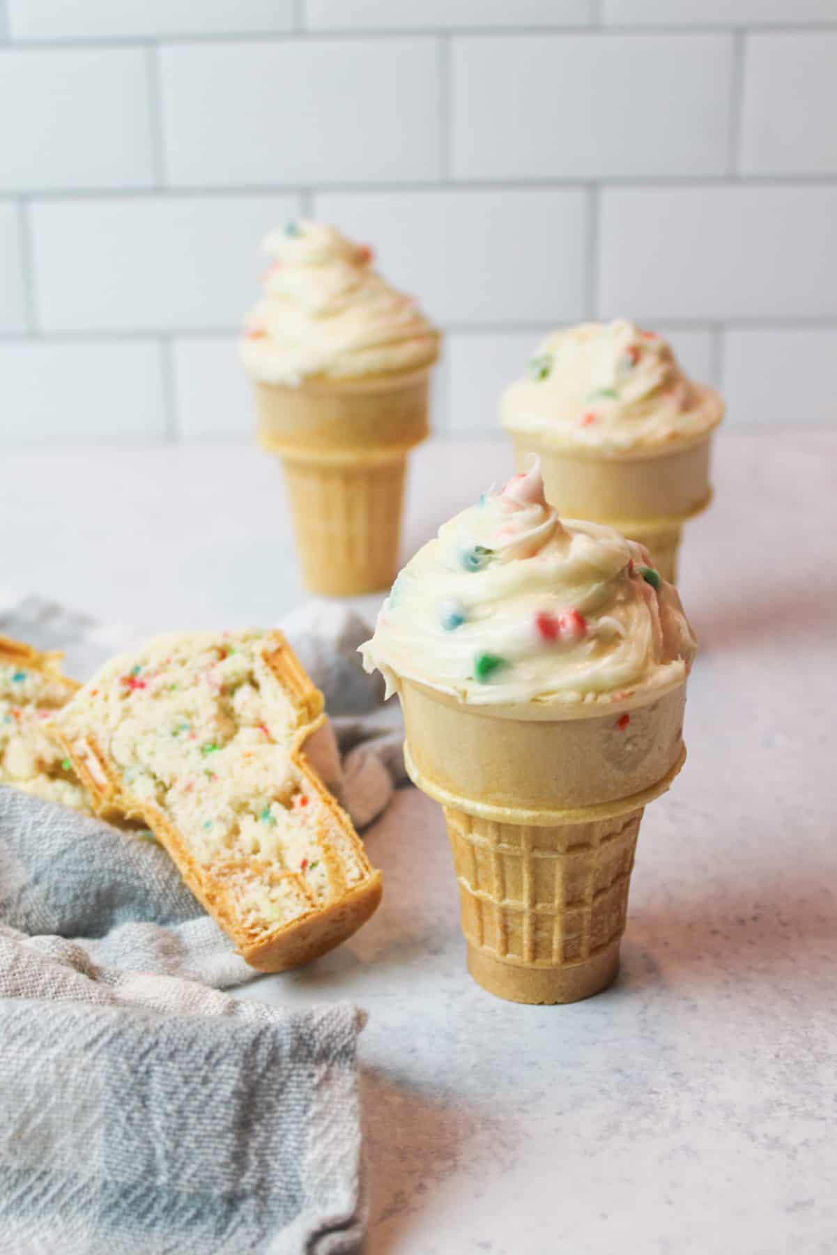 ice cream cone cupcakes with frosting and one cone split in half to reveal cake inside.