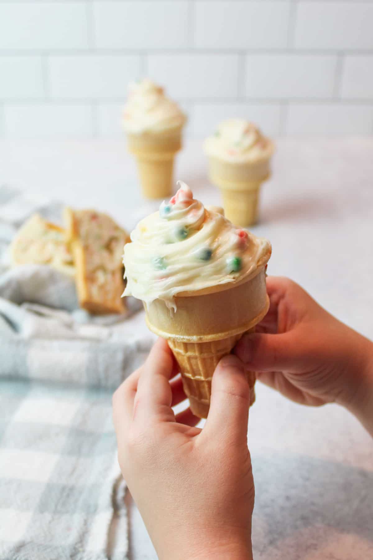 kid hands holding up a frosted cupcake ice cream cone.