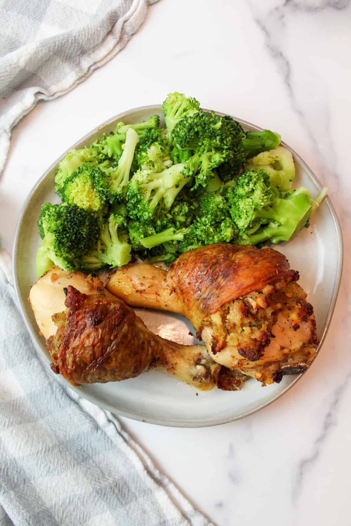 a plate filled with two stuffed chicken legs and steamed broccoli.