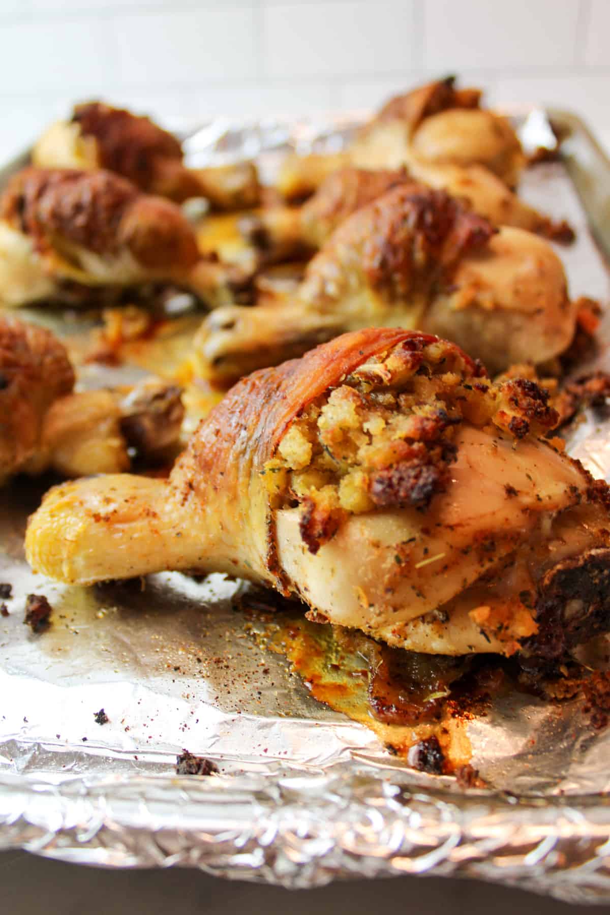 baked stuffed chicken leg on a foil lined baking sheet with more stuffed chicken in the background