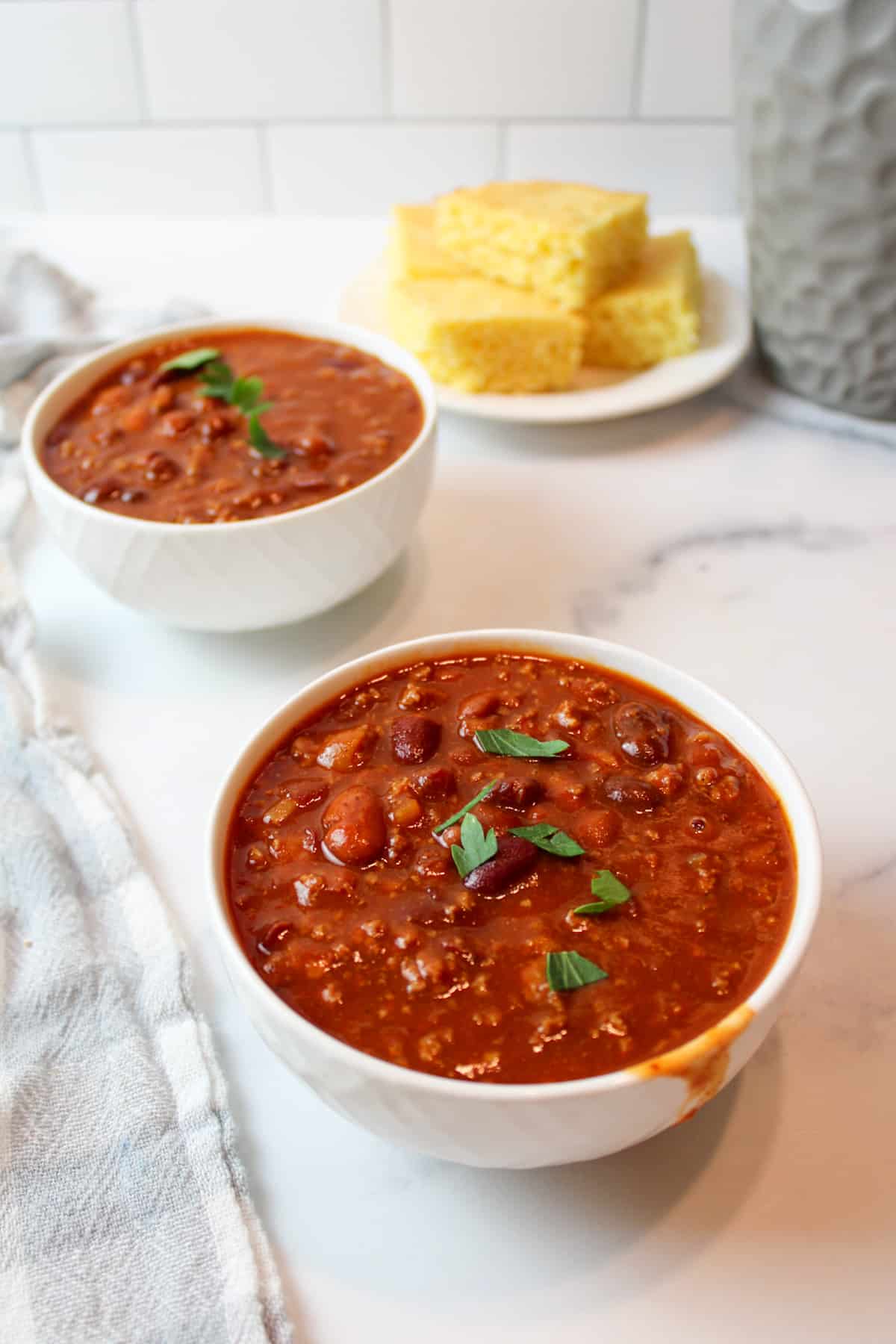 two bowls of tomato soup chili with a plate of cornbread in the background.