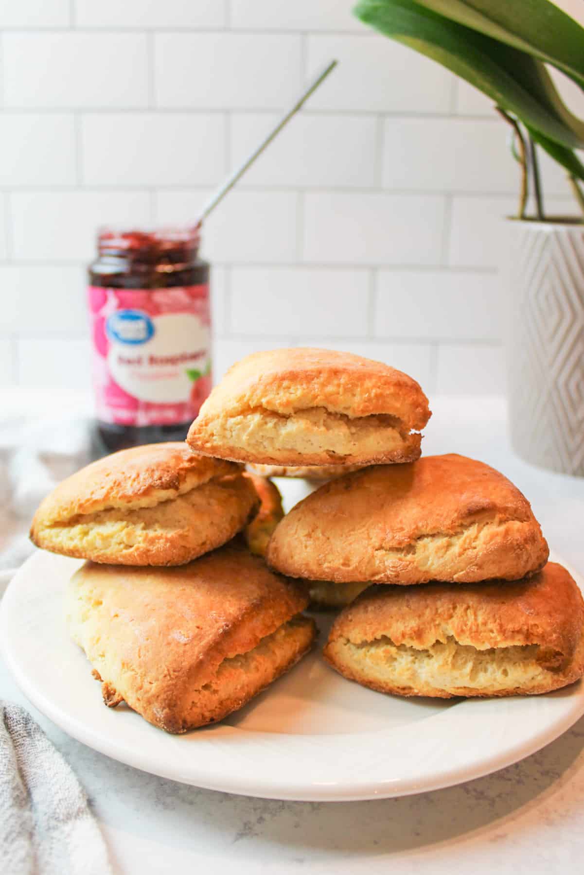 a stack of scones on a white plate with a jar of jam in the background