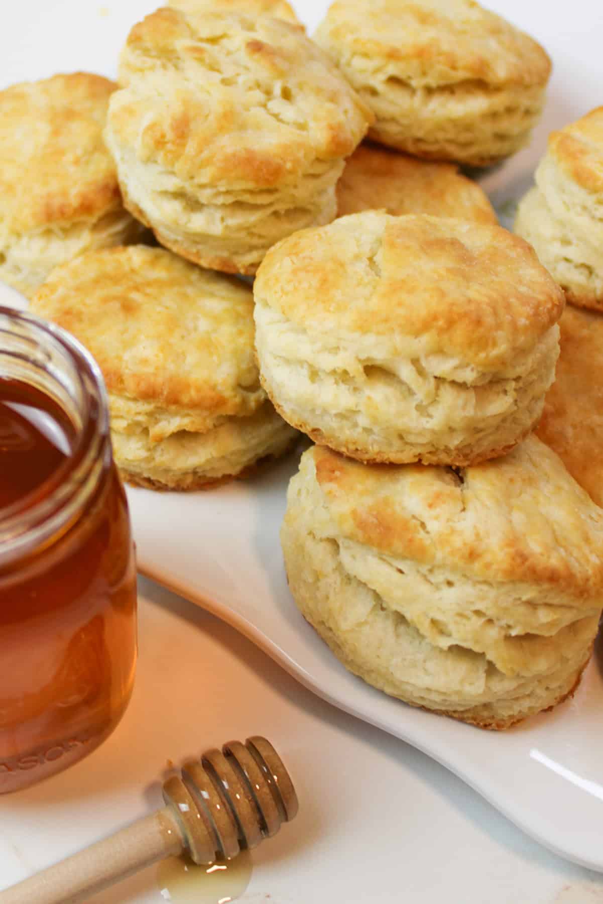 golden biscuits on a white plate next to jar of honey.