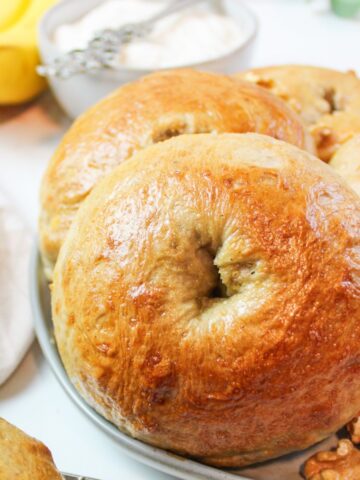 a banana nut bagel on a plate with more bagels and walnuts.