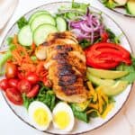 sliced chicken breast on a bed of lettuce surrounded by fresh veggies ad toppings.
