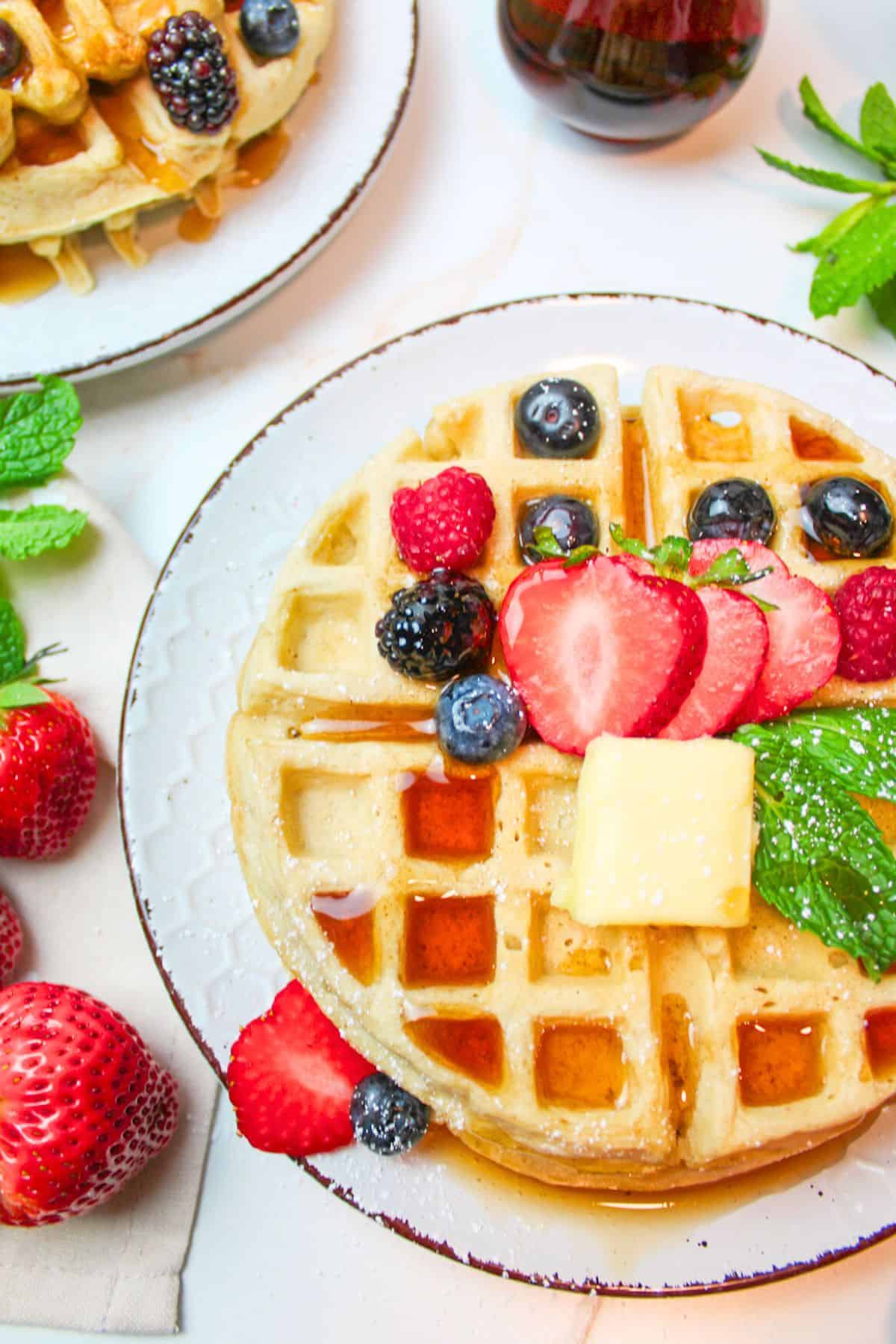 stacked waffles on a plate topped with butter, maple syrup, and fresh berries.