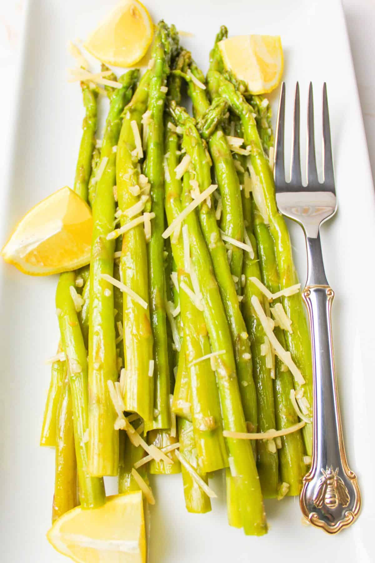 asparagus on a plate with a fork and lemon wedges.