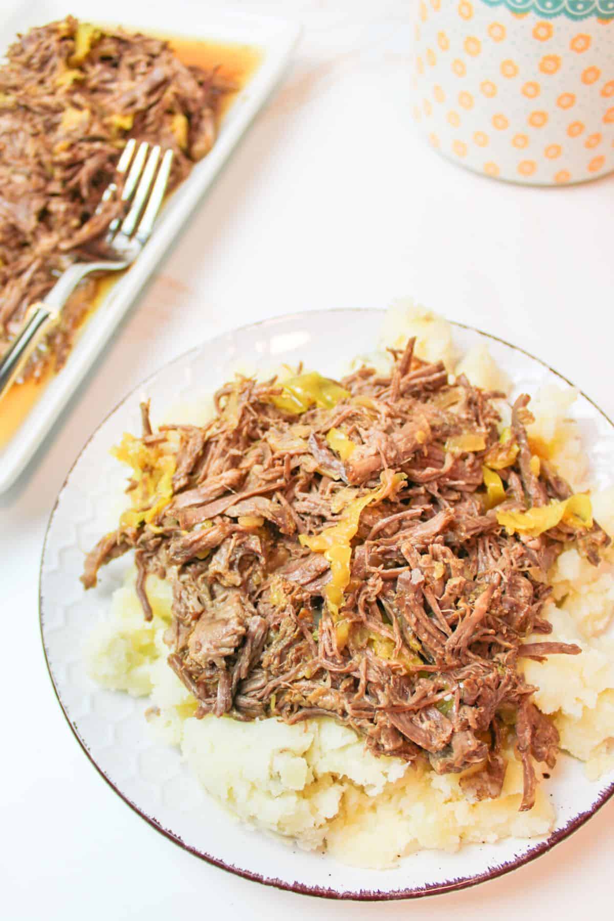 a plate with a bed of mashed potatoes topped with shredded mississippi roast.