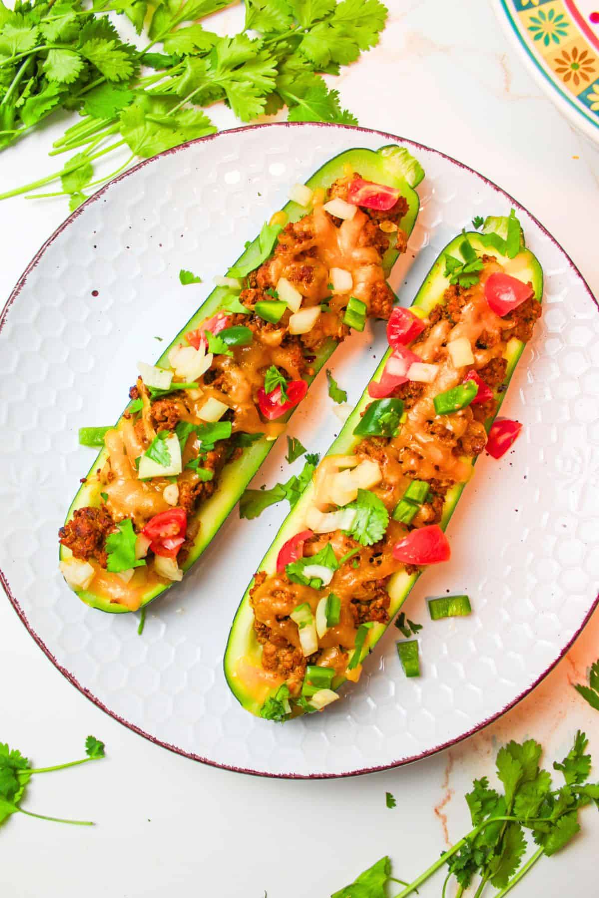 two zucchini taco boats on a plate with toppings.