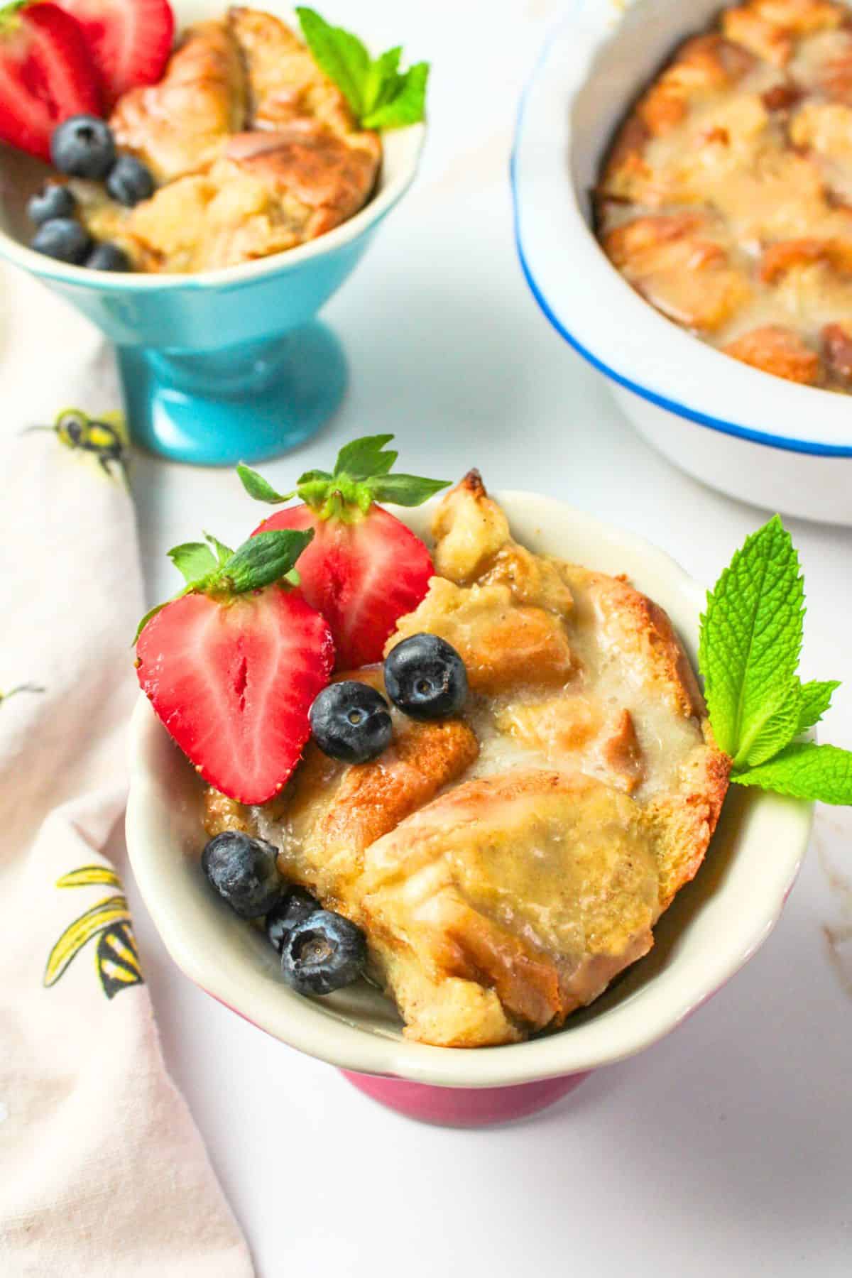servings of bread pudding in bowls with fresh fruit and mint leaf garnish.