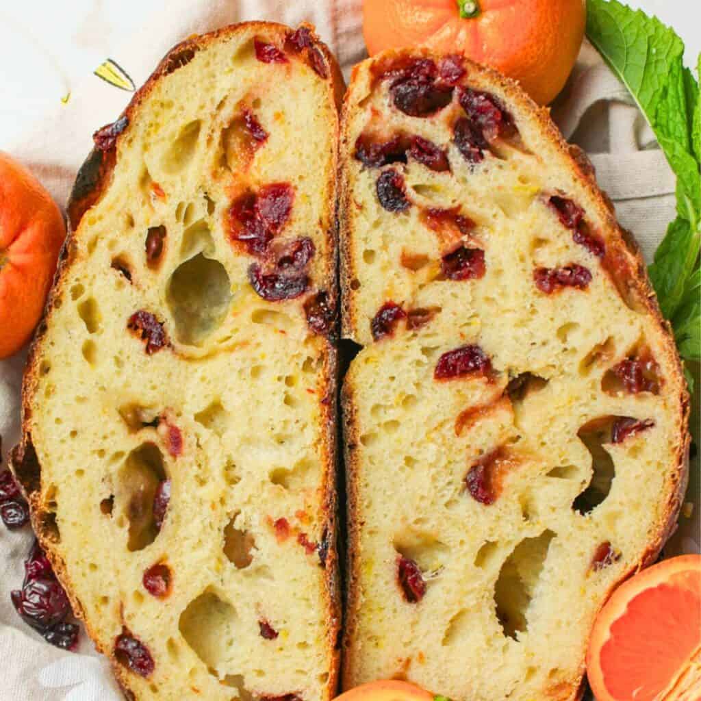 two halves of sliced cranberry orange sourdough loaf with fresh oranges beside them.